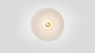Cielo wall light in satin brass, front view with a fritted glass disc lit