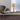 Ring table lamp in satin brass on a windowsill beside a grey leather armchair