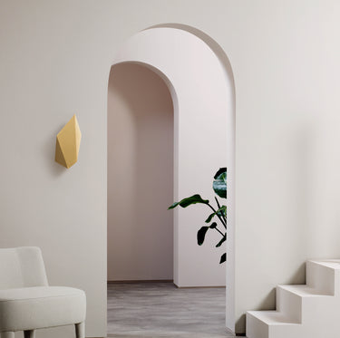 Abstract wall light, a brass leaf shape, on a pale wall beside an arched doorway