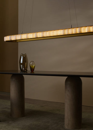 Avalon Oval chandelier in satin brass with alabaster segments, hanging over a dark dining table with two glass vases