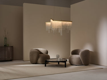 Cascata chandelier with hanging glass panels above a low table between two armchairs in a living room