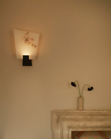 Relic wall light with a tall honed alabaster shade on a dark metal base, above a stone mantel