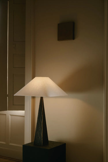 Cubist table lamp with a white linen pyramid shade on a dark cast bronze base, on a plinth by a wall panel