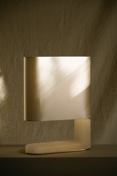 Columbo alabaster table lamp with a curved shade on a plinth against a draped backdrop