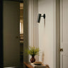 Heron wall light with a cylindrical shade on a short arm, in a room setting