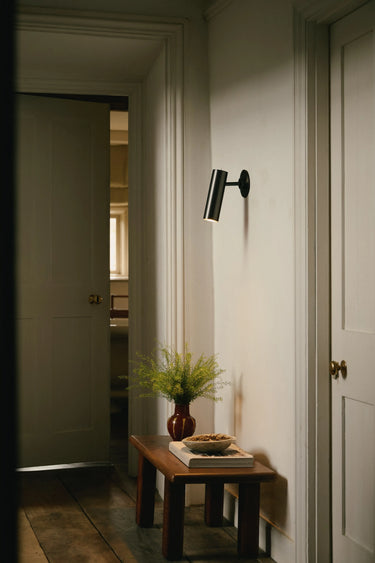 Heron wall light with a cylindrical shade on a short arm, in a room setting