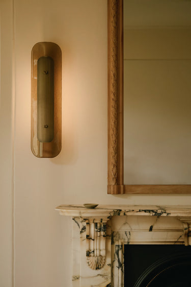 Contour wall light with textured glass beside a mirror above a fireplace
