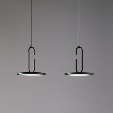 Two matt black Penta Clip pendants with open rings hanging side by side against a gray wall