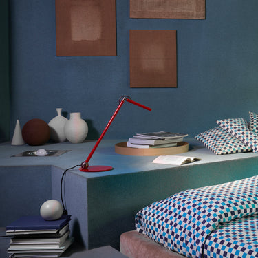 Scarlet red Oluce Calamaio desk lamp on a bedside shelf beside books
