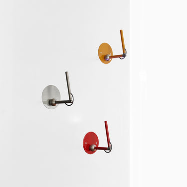 Oluce Calamaio wall lamp in satin black nickel, scarlet red and mustard yellow on a white background