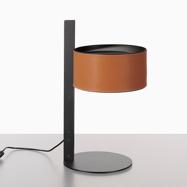 Oluce Parallel table lamp with a leather brown hammered leather shade on a matt black stem against a white studio background