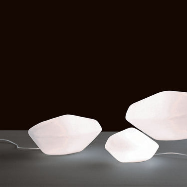 Oluce Stones outdoor lamps in white polyethylene glowing on a dark studio background