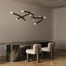 Trace Linear chandelier with crossing bronze strands and glass tips above a long dark oval dining table with cream chairs