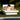 White resort bed with tan pillows beside a pool and lawn, part of the Spa Club Now cabana set