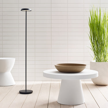 Black Tepa Medium cordless floor lamp by Sean Lavin glowing beside a round white table in a bright room