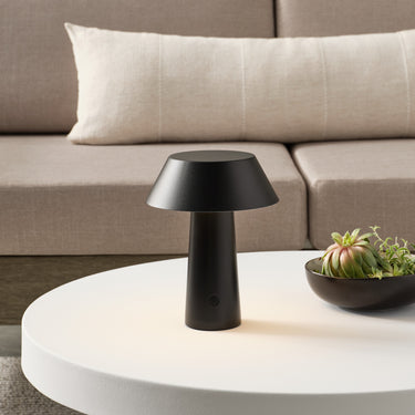 Sesa Short Accent rechargeable table lamp in Black glowing on a white round table beside a sofa