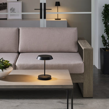 Black Tepa Short Accent table lamp lit on a coffee table in front of an outdoor sofa