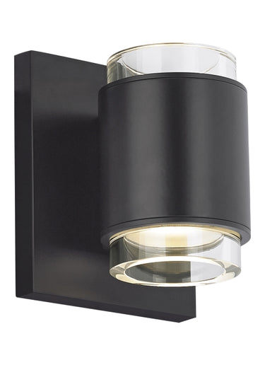 Voto modern round LED wall light in black finish, illuminated with warm 3000K light, mounted vertically on a hallway wall.