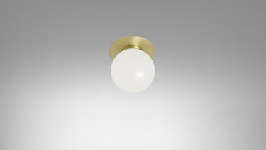 Small Mezzo flush light with a round opal glass globe and a satin brass backplate, studio view