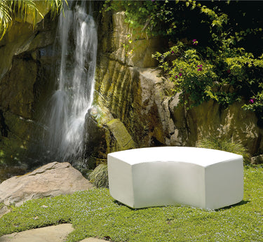 White Arc curved bench on a lawn in front of a rock wall and waterfall