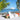 White Puck round ottoman beside a Check chair with a colorful throw on a beach with sailboats