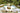 Pair of white Cot twin daybeds with striped pillows and a fruit basket beside a garden pond with palms