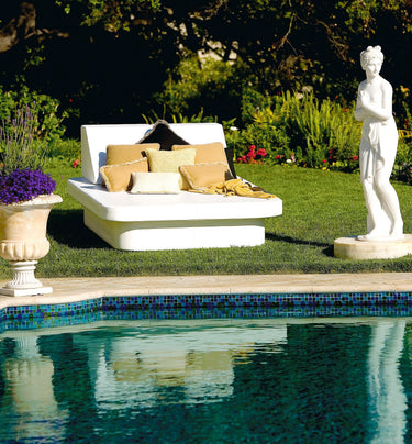 White Crib queen daybed with Lean wedge headboards and tan pillows on a lawn beside a pool with a classical statue