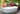 Moon Pad daybed with coral and green pillows beside a reflecting pond on a terrace
