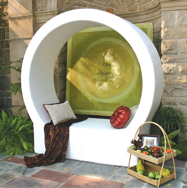 White Pod circle lounge on a stone terrace with a throw, a tufted red pillow and a fruit basket beside it