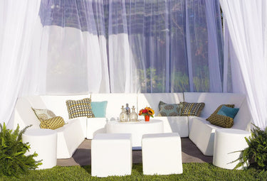 Romp Club Now cabana set in white vinyl: a U-shaped sectional of lounge chairs and corner modules with ottomans on a lawn under sheer curtains