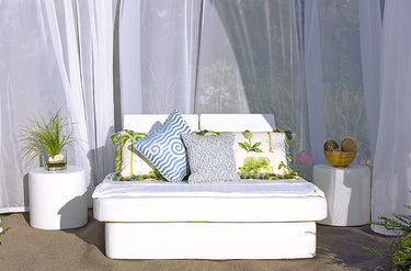 Spa Club Now cabana set with a white queen resort bed, patterned pillows and two cylinder ottoman side tables under sheer curtains