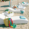 Row of white Surf sun lounges with colorful towels and bags on a sandy beach