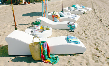 Row of white Surf sun lounges with colorful towels and bags on a sandy beach