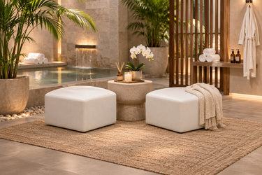 Two Zest corner ottomans in white vinyl beside a stone pedestal table in a candlelit spa courtyard