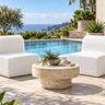 Two Zig armless chairs in pale vinyl facing each other across a travertine drum table beside a pool