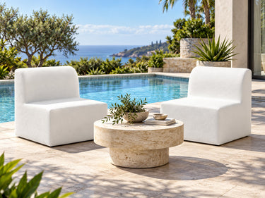 Two Zig armless chairs in pale vinyl facing each other across a travertine drum table beside a pool