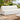 Zig Duo continuous-back bench in white vinyl on a garden terrace, with a stone side table and olive trees behind
