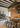 Two Ilo horizontal pendants over a long dining table in a loft with wood shelving and beams
