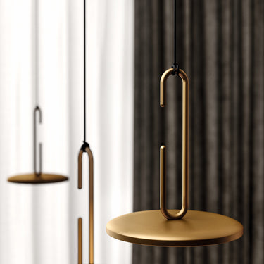 Matt gold Penta Clip pendant with its open ring hooked to the cable above a glowing disc