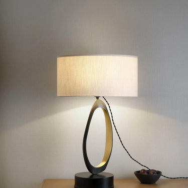 Stella table lamp with a linen drum shade on a wooden sideboard beside a small bowl against a grey wall