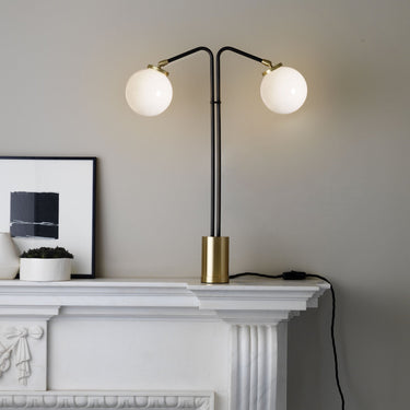 Array twin table lamp with two lit opal glass globes beside a fireplace