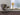 Ring table lamp in satin brass on a windowsill beside a grey leather armchair