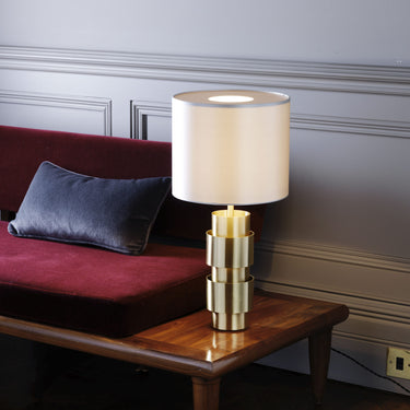 Ring table lamp in satin brass on a wood side table beside a red velvet sofa