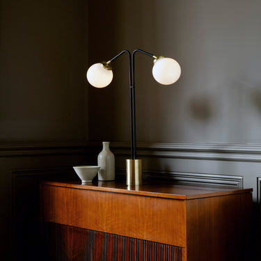 Array twin table lamp with two lit opal glass globes in a dark room