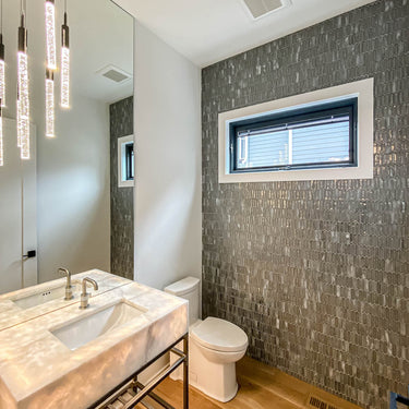 ET2 Big Fizz lit bubble glass pendants hanging beside a mirror in a powder room with a stone vanity and gray tiled wall