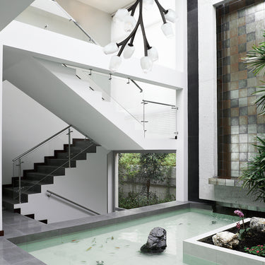 ET2 Blossom black branch pendant hanging down a bright stairwell beside an indoor pond
