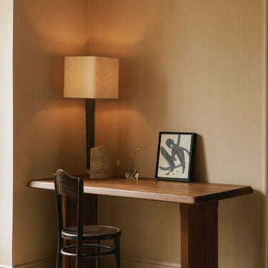 Roc table lamp glowing in a corner on a timber desk beside framed abstract art and a bentwood chair