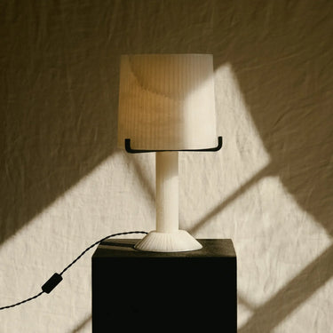 Acropolis table lamp on a plinth against a draped backdrop with its black cord