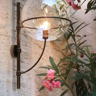 Lyndon outdoor wall lamp by Oluce mounted near flowering plants, lifestyle view