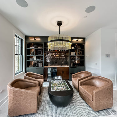ET2 Chimes tube-ring pendant in Black and Satin Brass hanging over a seating area in a den with built-in shelves and brown leather chairs